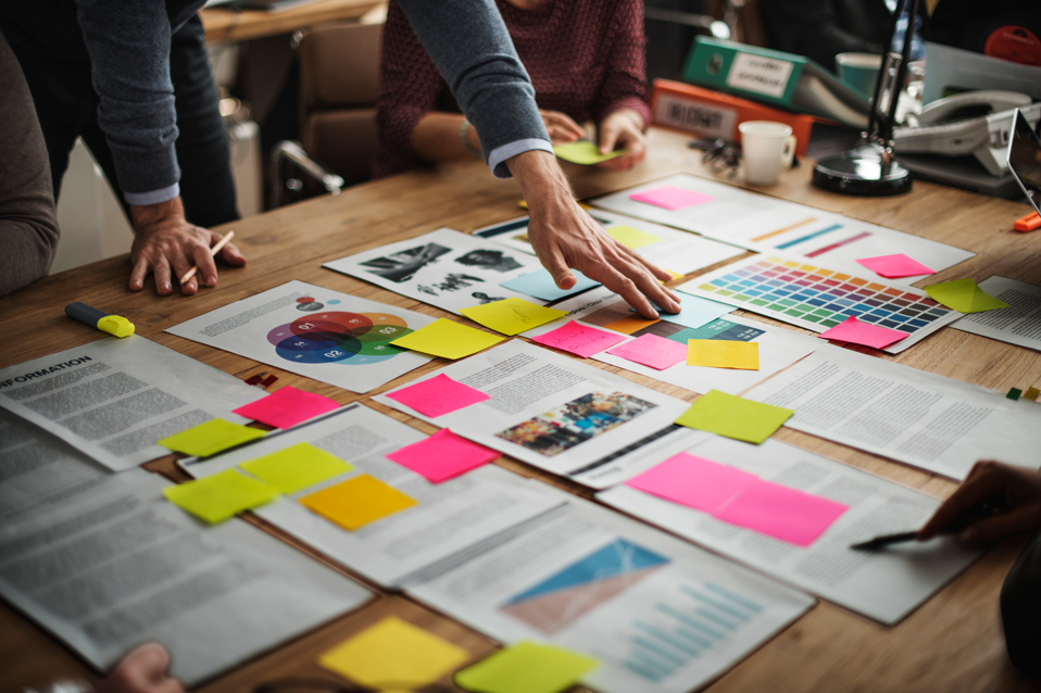 sur une table sont éparpillés des papiers et post-its et une personnes les regarde et semble vouloir les déplacer