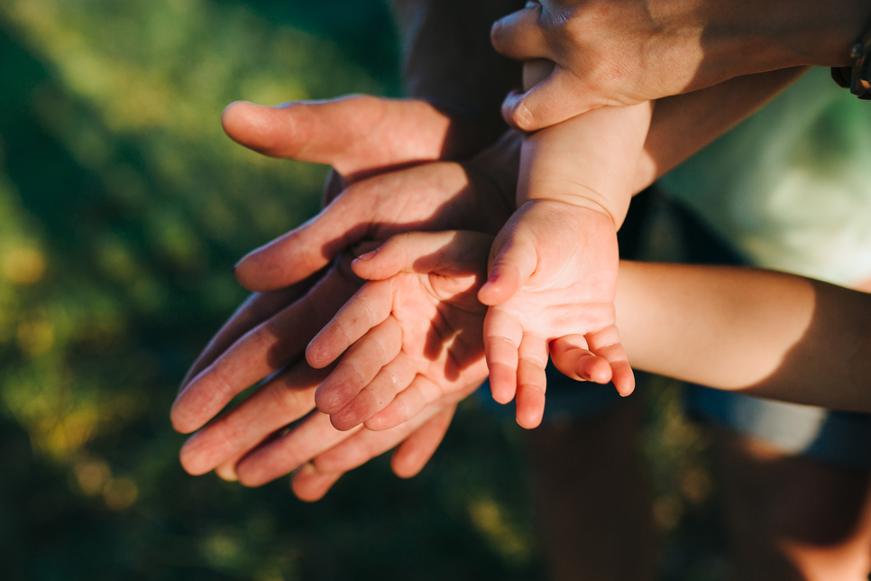 Plusieurs mains se superposent, des mains d'adultes, d'enfants et de bambin.