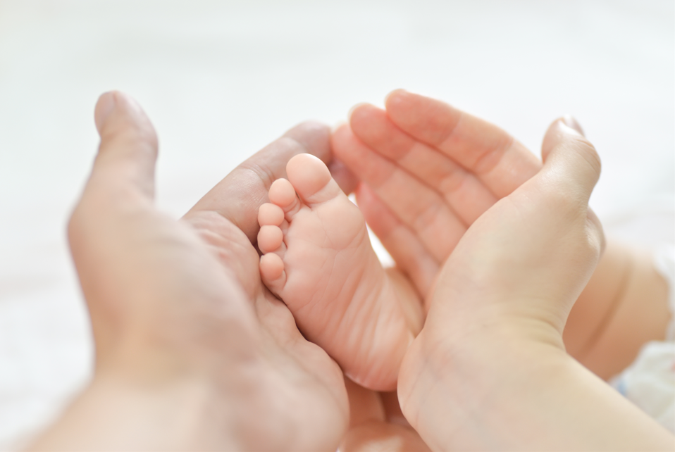 Les mains d'un adultes tiennent tendrement le pied d'un bébé