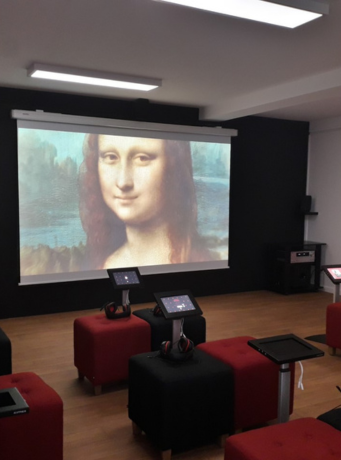 salle avec une oeuvre projeté sur un écran, des tablettes, ...