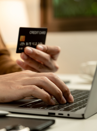 Main d'une personne tenant une carte bancaire et utilisant un ordinateur portable